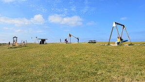 A grassy field with various playground equipment including swings, a slide, and a climbing structure. - Beautiful holiday home with courtyard (Ravenoville-Plage)