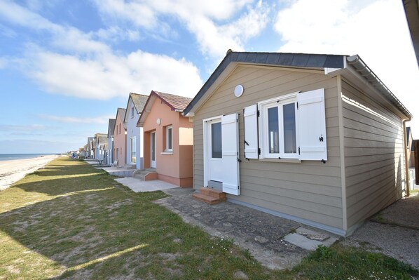 A row of beachside cottages with a grassy lawn and a beach in the background. - Beautiful holiday home with courtyard (Ravenoville-Plage)