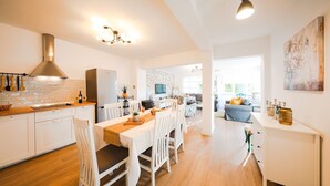 Una cocina moderna con armarios blancos, una isla central y una zona de comedor con sillas blancas y una mesa de madera.