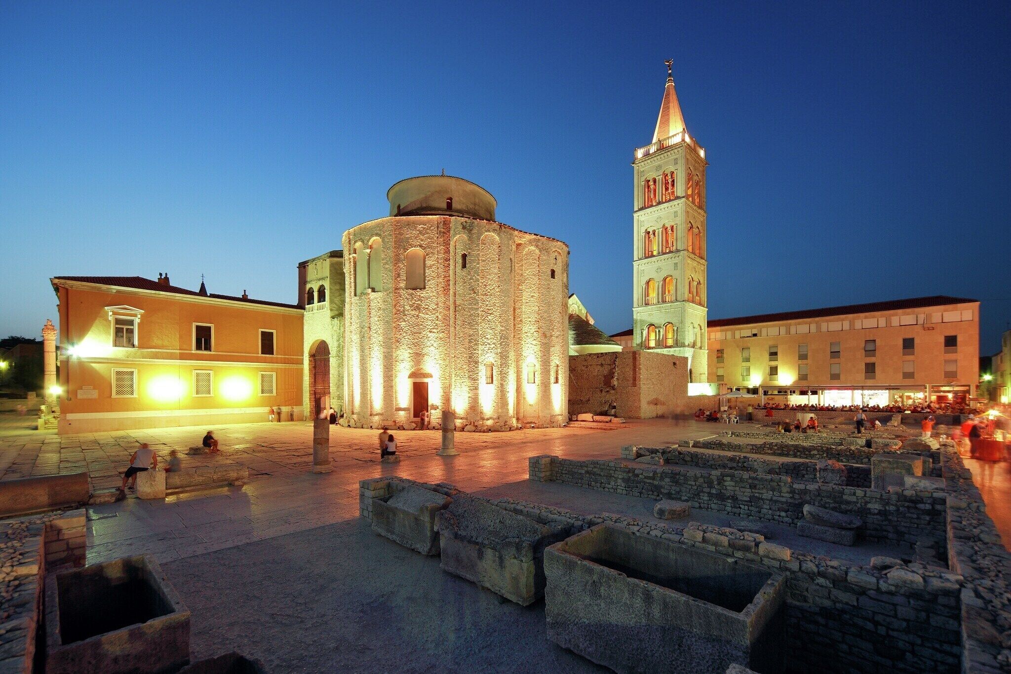 A historical square with a round building and a tall tower, surrounded by stone walls and open space.