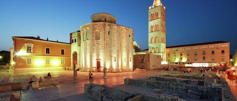 A historical square with a round building and a tall tower, surrounded by stone walls and open space.