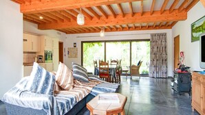 Amplia sala de estar con techo de madera, un sofá con cojines a rayas, una mesa de centro y un comedor con sillas y una mesa.