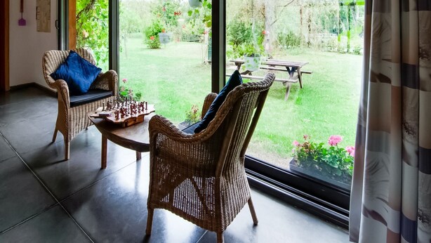 Una habitación con muebles de mimbre, un tablero de ajedrez y vistas a un jardín a través de amplias ventanas.