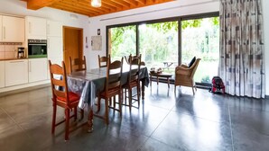 Una cocina amplia con electrodomésticos modernos, un comedor con mesa y sillas, y ventanas grandes con vistas a la vegetación.