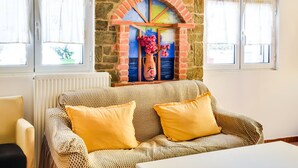 A cozy room with a patterned sofa, yellow cushions, a vase with flowers, and a brick wall with a colorful window design. - Alluring Holiday Home in Syros with Barbecue (Syros)