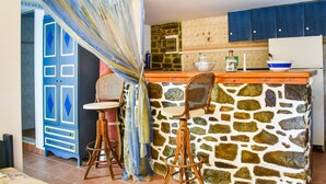 A kitchen with a stone wall, a wooden bar counter, two bar stools, and a blue cabinet. - Alluring Holiday Home in Syros with Barbecue (Syros)