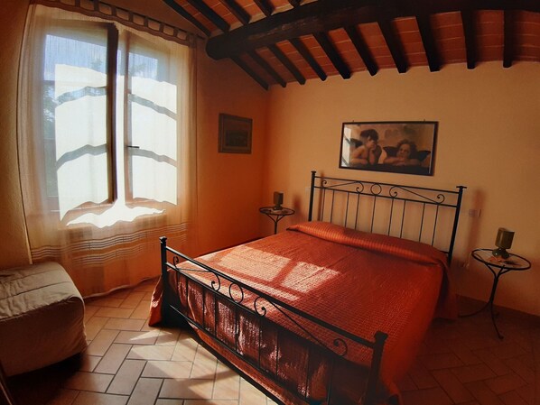 A bedroom with a bed, a window, a painting, and a small table.