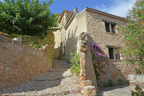A stone staircase leading to a rustic building with a tiled roof, surrounded by greenery and flowering plants.