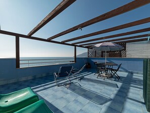 Une terrasse avec une table et des chaises, une chaise verte et une vue sur la mer.