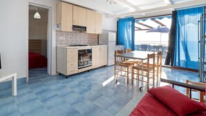 A compact kitchen with a dining area, a red sofa, and a view of the sea through large windows.