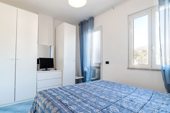 A bedroom with a bed, a TV on a dresser, a window with curtains, and a wardrobe.