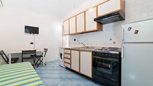 Ett kompakt kök med spis, ugn, tvättmaskin och en liten matplats med bord och stolar.