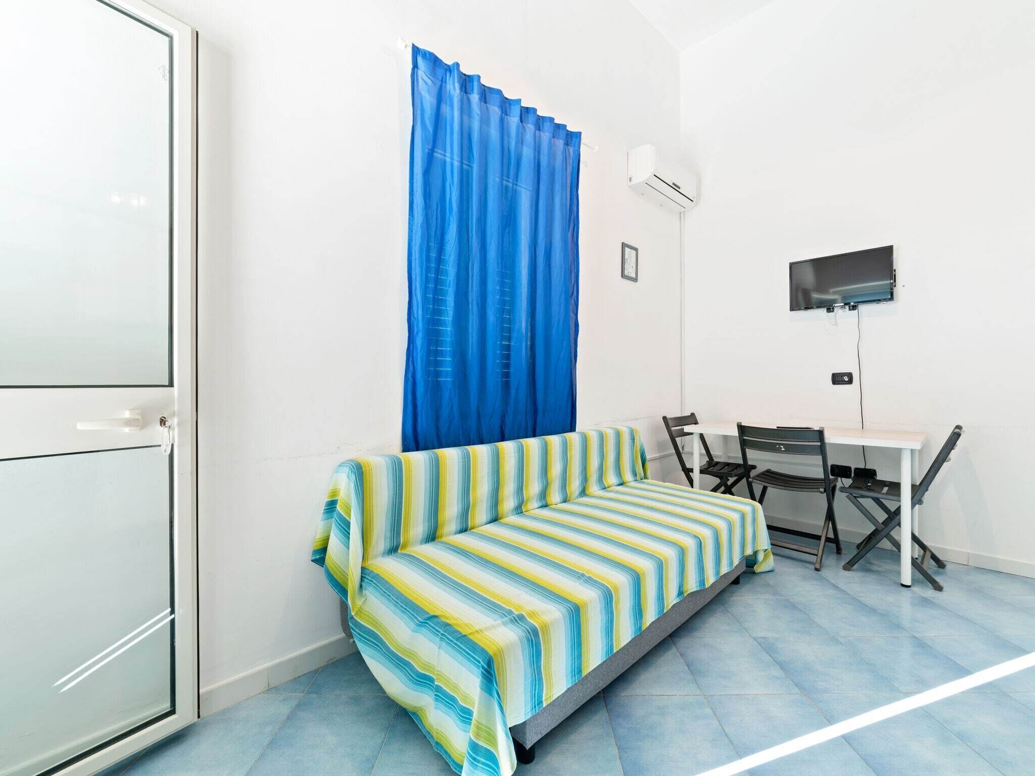Une petite pièce avec un canapé à rayures, un bureau, une chaise, un téléviseur et un appareil de climatisation.