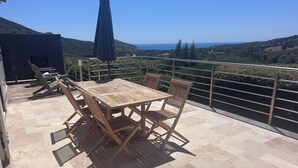 A wooden table and chairs on a balcony with a view of the sea and hills. - Villa with pool, between olive trees and sea - fantastic view! (Cargèse)