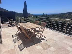 A wooden table and chairs on a balcony with a view of the sea and hills. - Villa with pool, between olive trees and sea - fantastic view! (Cargèse)