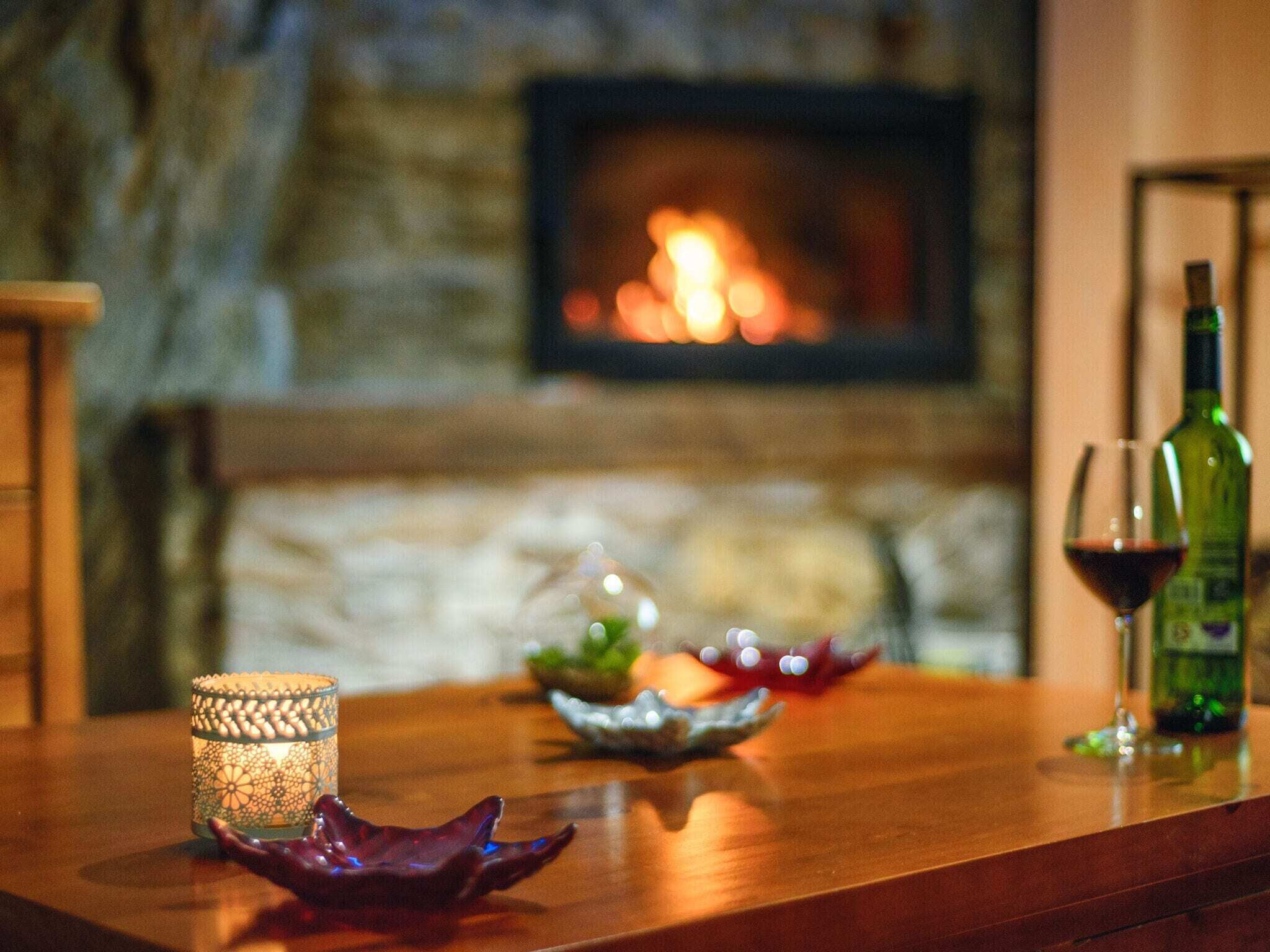 A wooden table with a candle, a glass of red wine, and a bottle of wine.