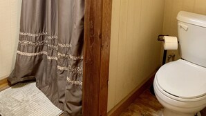 Une salle de bain avec un rideau de douche, des toilettes et une étagère en bois au-dessus des toilettes.