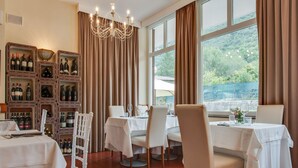 A restaurant with white tables and chairs, a wine display, and large windows with curtains. - Family escape with Pools and Sauna (Foligno)
