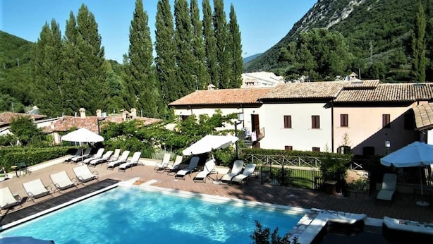 A swimming pool with lounge chairs and umbrellas, surrounded by buildings and trees. - Family escape with Pools and Sauna (Foligno)
