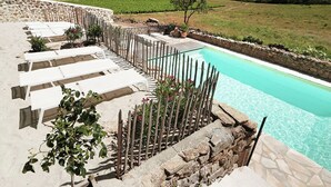 A pool area with white lounge chairs and a stone wall. - Blissful Stay in Mandourelle (Villesèque-des-Corbières)