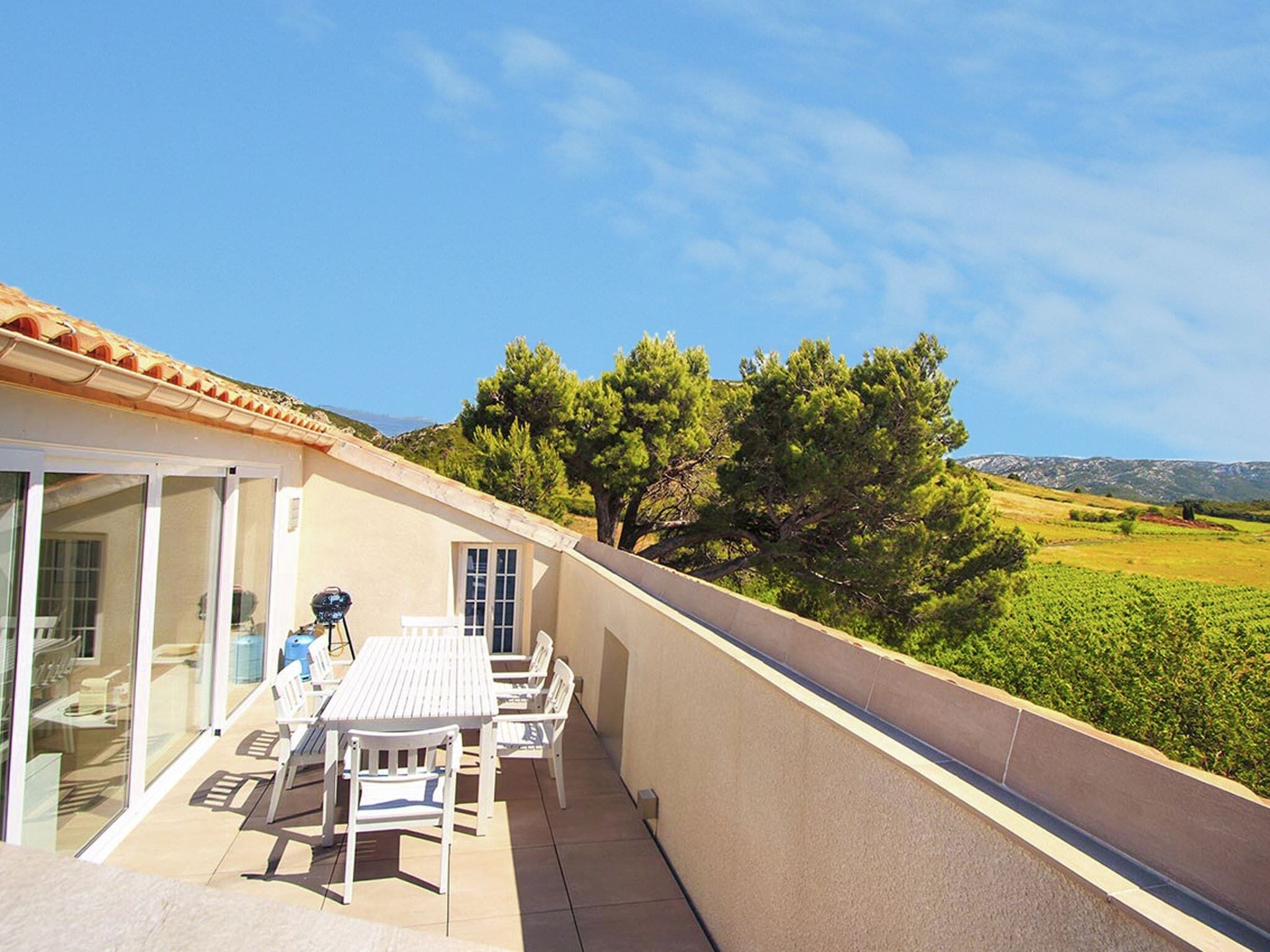 A balcony with a table and chairs, overlooking a green landscape and distant mountains.