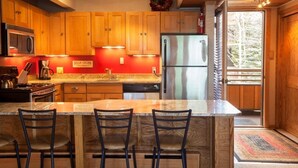 A modern kitchen with wooden cabinets, a stainless steel refrigerator, and a central island with bar stools. - Laurelwood, A Destination Residence (Snowmass Village)