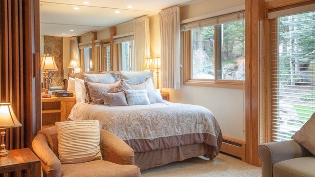 A spacious bedroom with a large bed, bedside tables, and a view of the outdoors through large windows. - Laurelwood, A Destination Residence (Snowmass Village)