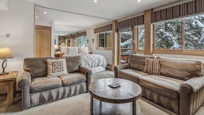 A modern living room with leather sofas, a round coffee table, and large windows with a snowy view. - Laurelwood, A Destination Residence (Snowmass Village)