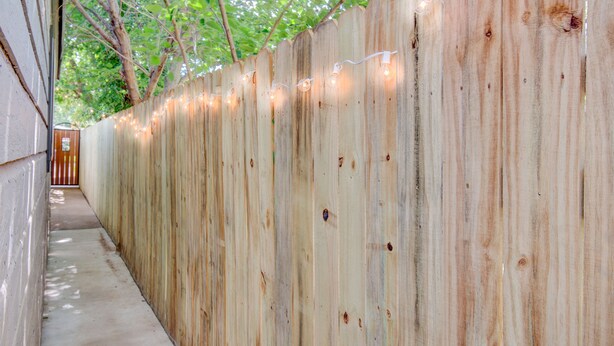A wooden fence with string lights, a concrete pathway, and a tree in the background. - ⫷1 BD/1 Bath⫷Tiny Magnolia Retreat⫷⫸Near TTU⫸ (Lubbock)