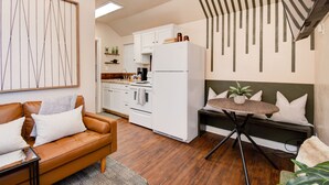 A modern kitchen with white cabinets, a refrigerator, and a dining area with a bench and table. - ⫷1 BD/1 Bath⫷Tiny Magnolia Retreat⫷⫸Near TTU⫸ (Lubbock)