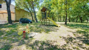 A playground with a slide and climbing structure, surrounded by trees and a parked car.