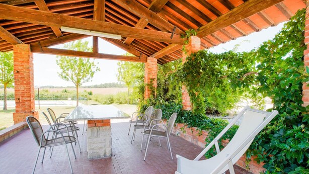 An outdoor patio with a brick floor, a wooden pergola, and a table surrounded by metal chairs.