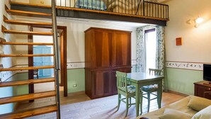 Une pièce comprenant un escalier en bois, une table à manger avec des chaises, un coin cuisine et un canapé.