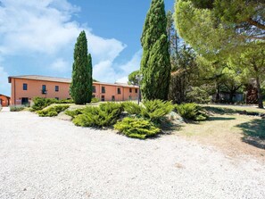 Un edificio con vialetto sterrato, circondato da siepi curate e alberi alti.