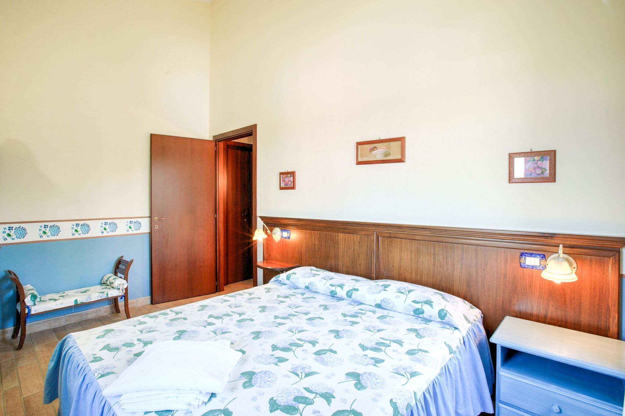 A bedroom with a bed, bedside table, bench, and a door.