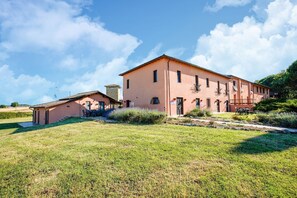 Un edificio ampio con tetto piatto e numerose finestre, circondato da un prato curato e una piccola costruzione a sinistra.