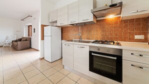 A modern kitchen with white cabinets, a gas stove, an oven, and a sink. There is a sofa and a chair in the adjacent living area. - Apartment in Agropoli with garden (Agropoli)