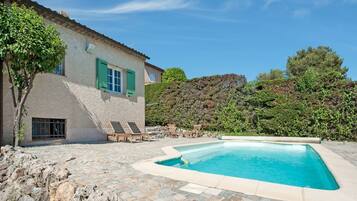 Une maison avec une piscine, une terrasse en pierre et une vue sur une colline en arrière-plan.