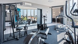 A modern gym with various exercise equipment, large windows, and a view of the outdoors.