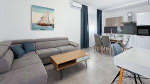 A modern living room with a grey sofa, a wooden coffee table, and a dining area with a white table and chairs.