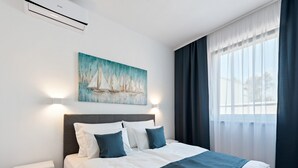 A modern hotel room with a neatly made bed, a painting of sailboats on the wall, and a view of the city through the window.