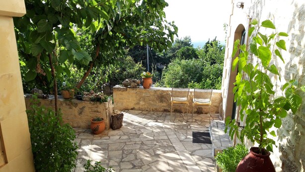 Un patio con suelo de piedra, plantas en macetas y sillas de mimbre.