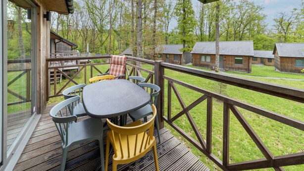 Un terrazzo in legno con tavolo e sedie, affacciato su una zona verde con alcune cabine.