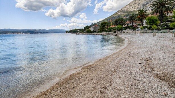 A pebble beach with clear water, a mountain in the background, and buildings with red roofs. - Villa in Orebić near Sea Beach (Orebić)