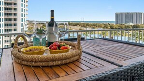 Ein Korbstuhl mit einer Weinflasche, zwei Weingläsern und einer Schale Erdbeeren auf einem Balkon mit Blick auf ein Gewässer und Gebäude.