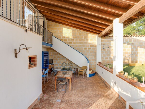 Un patio techado con techo de madera, pared de ladrillo y escalera de caracol.