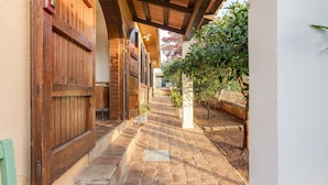 A covered outdoor corridor with wooden doors and a brick pathway leading to a building entrance.