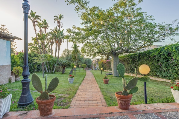 Un chemin de jardin bordé de cactus en pot, de palmiers et d’une allée pavée en briques.