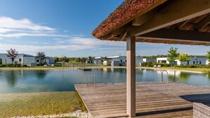 A modern outdoor pool area with a wooden deck, a covered seating area, and a clear view of the surrounding buildings. - Classy Holiday Home in Lutzmannsburg (Zsira)