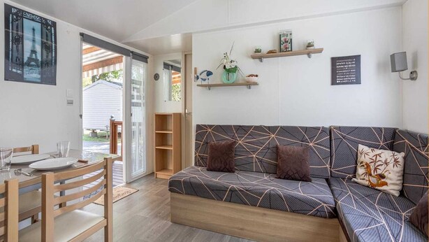 A modern living room with a sofa, a dining table with chairs, and a kitchen area visible through an open door.